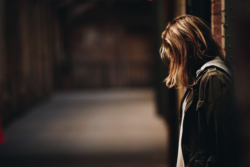 A young girl with short loose hair covering her face standing at a lonely nook.