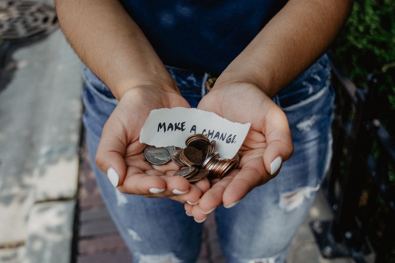 Woman hold out open hands full of change and a note that reads 