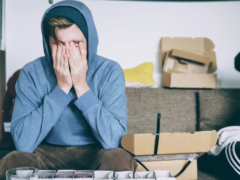 A stressed student wearing a hoodie holds face in their hands.