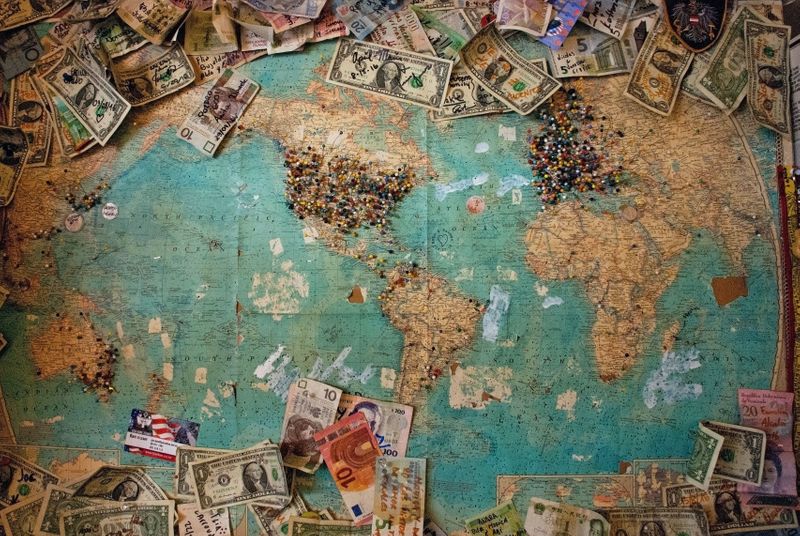 A micture of the world with different amounts of paper money pinned around it.