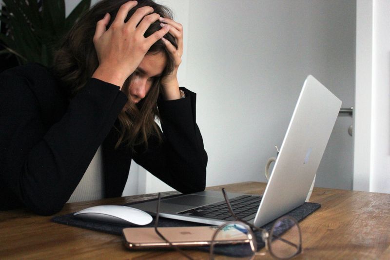 A woman in front of a laptop holds her head in her hands.