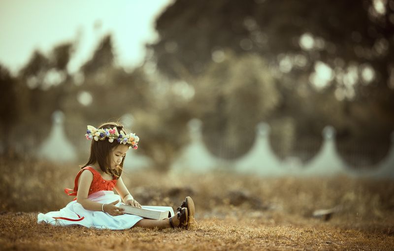 Young child sitting outdoors reading a book