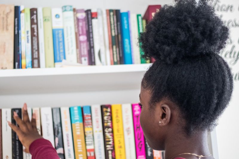 A girl looking at a book shelf of LGBTQ+ children's books