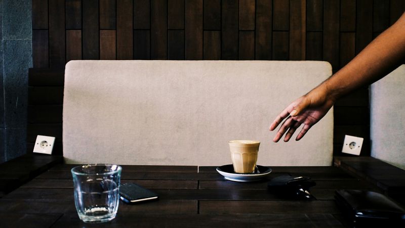 A hand taking a cup of coffee off of a desk.