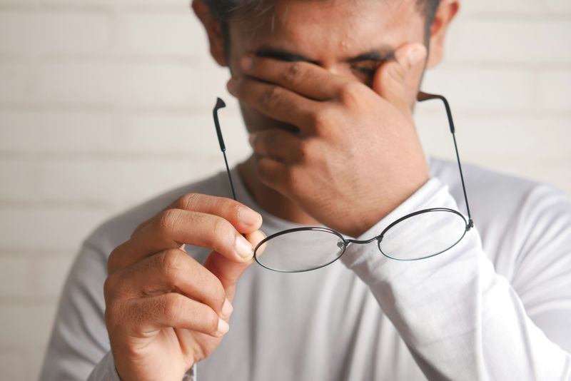 A person removing their eyeglasses with their right hand, and covering their eyes with their left hand.