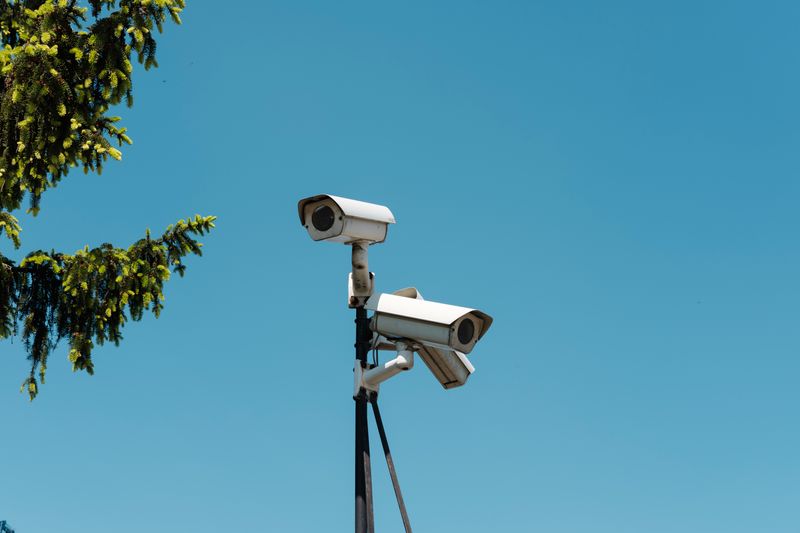 Three security cameras outdoors on top of a pole facing different directions. 