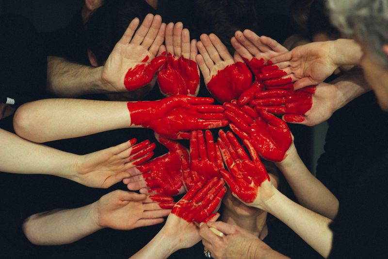 Red heart painted over a bunch of people's hands 