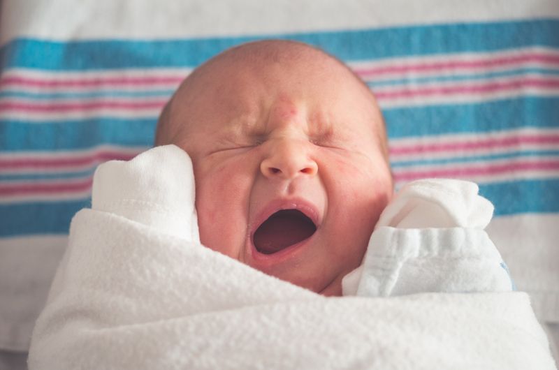 gender identity vs gender expression: Baby yawning with blue and pink blanket in the background.