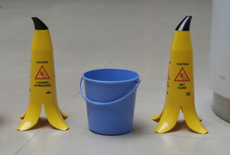Two caution signs on either side of a blue pail.