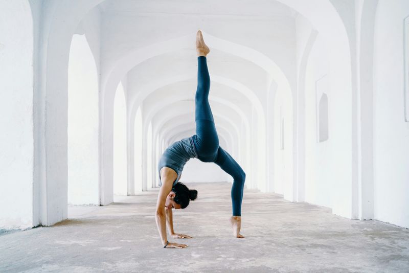 Woman doing a backbend in a white hall with arches.