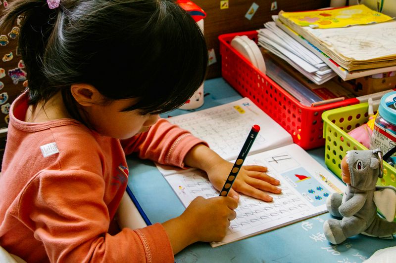 A little girl is tracing the number 4 in a workbook repeatedly