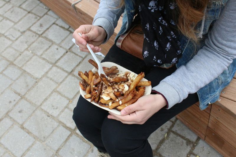 A person eating poutine in a takeout container.