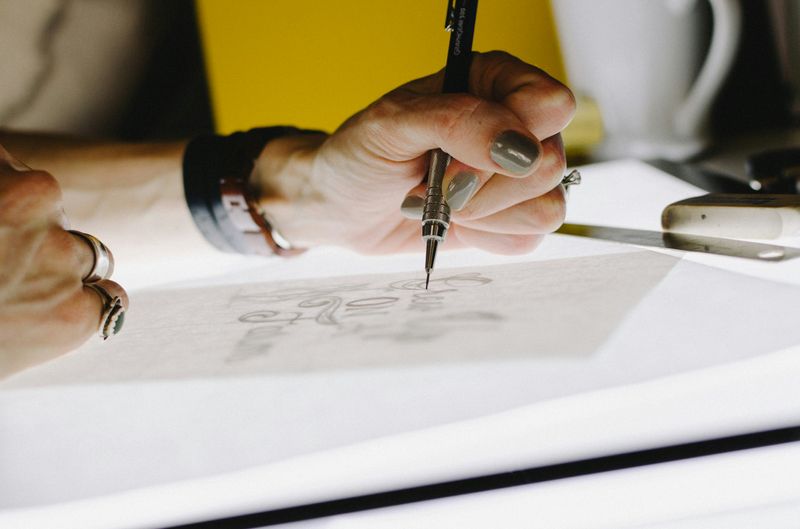 An artist drawing on paper with a pencil over a lit up table.