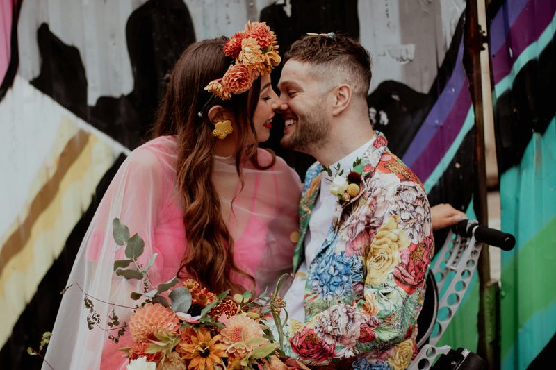 Two colorful people smile at each other with a bouquet of flowers.