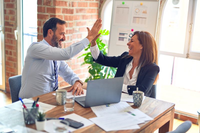 Man and woman happily giving one another a high-five in an office setting.