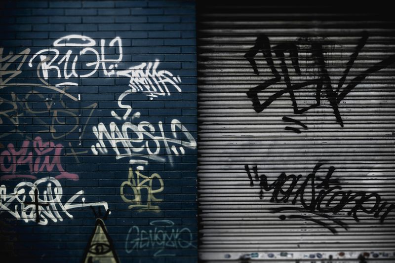 A garage door beside a blue brick wall with various graffiti tags drawn in different contrasting colors.