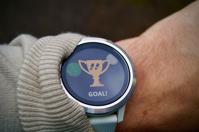 A person wearing a smartwatch with a trophy icon and the word “GOAL!” on screen, indicating a completed fitness target.