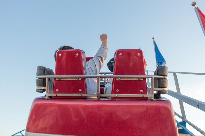 A roller coaster cart transporting two passengers, one putting his fist in the air. 