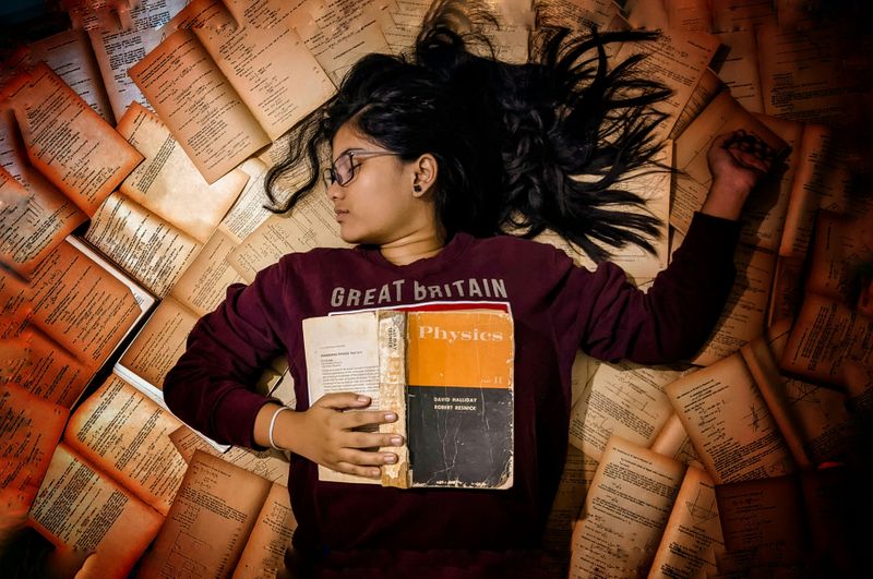 A woman laying on books surrounding her.