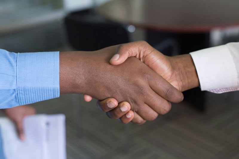 Two people shaking hands firmly over a desk in a office environment.