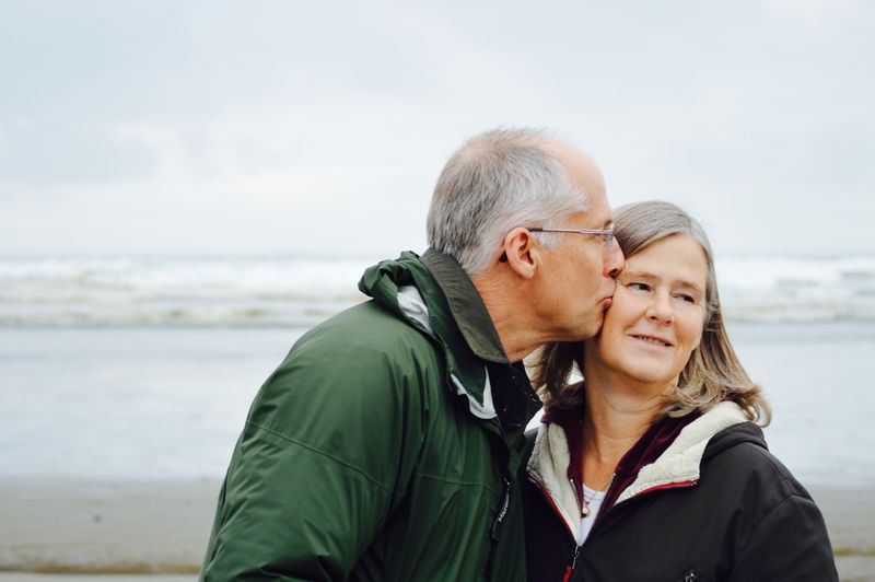 Photo of older man kissing older woman on side of her face.