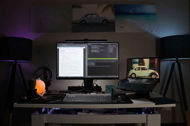 A desk with a computer monitor, keyboard, and laptop on a stand on top.