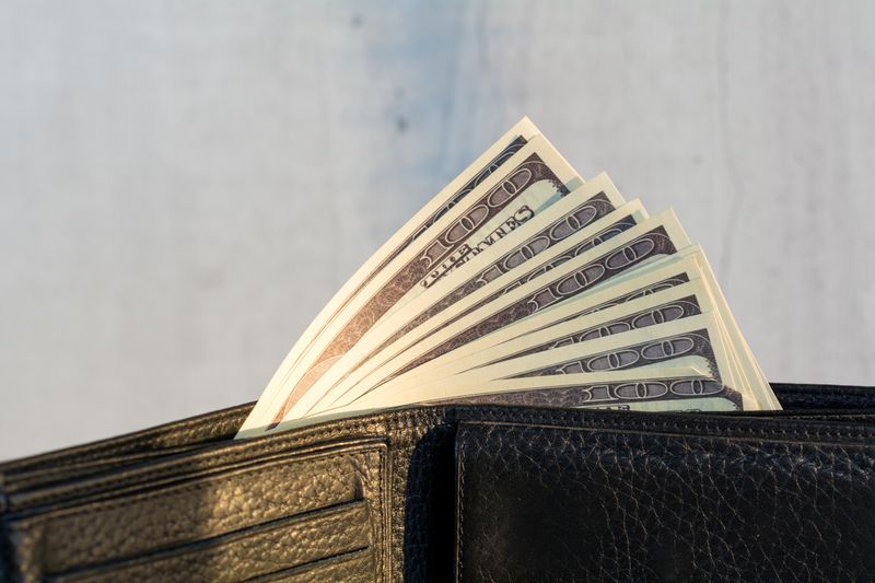 A black wallet filled with several hundred-dollar bills partially visible.