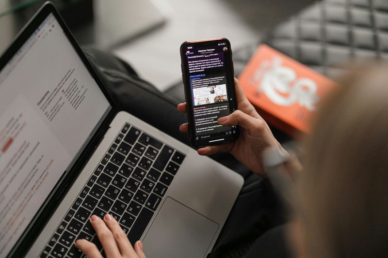 A person using a laptop and mobile phone.