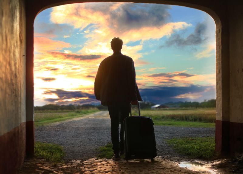 Young man leaving and pulling a rolling suitcase.