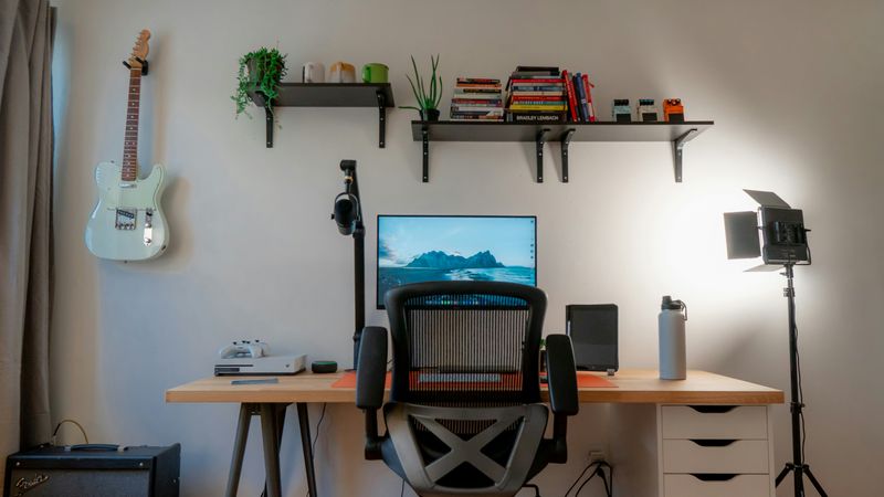 A person's home office desk, with a computer, microphone and light ready for a one-way video interview.