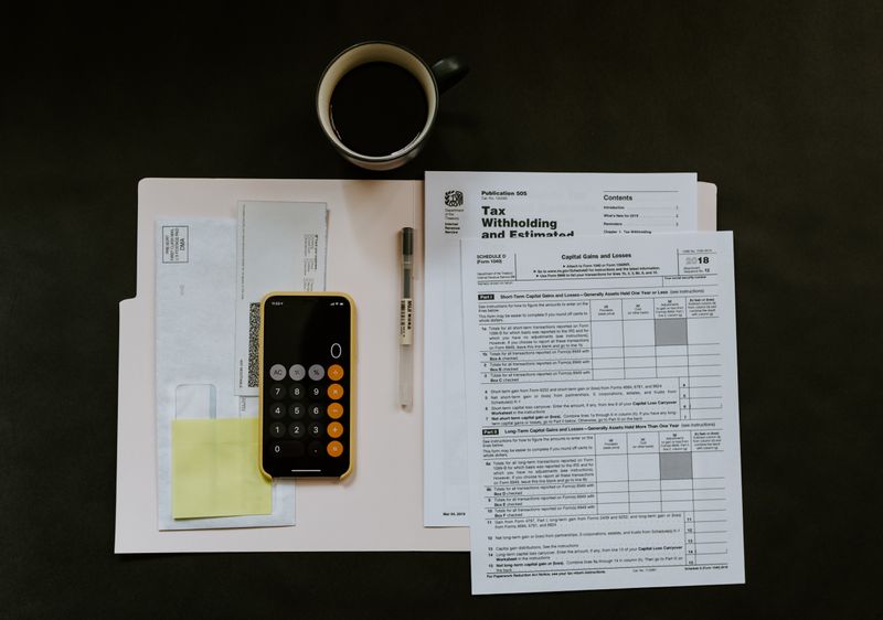 A calculator, pen, tax documents, and a coffee filled mug on a desk