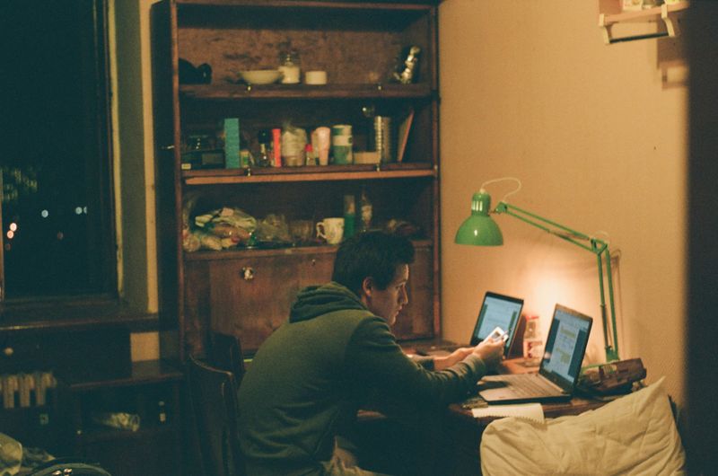 A young man typing ChatGPT prompts onto a laptop.