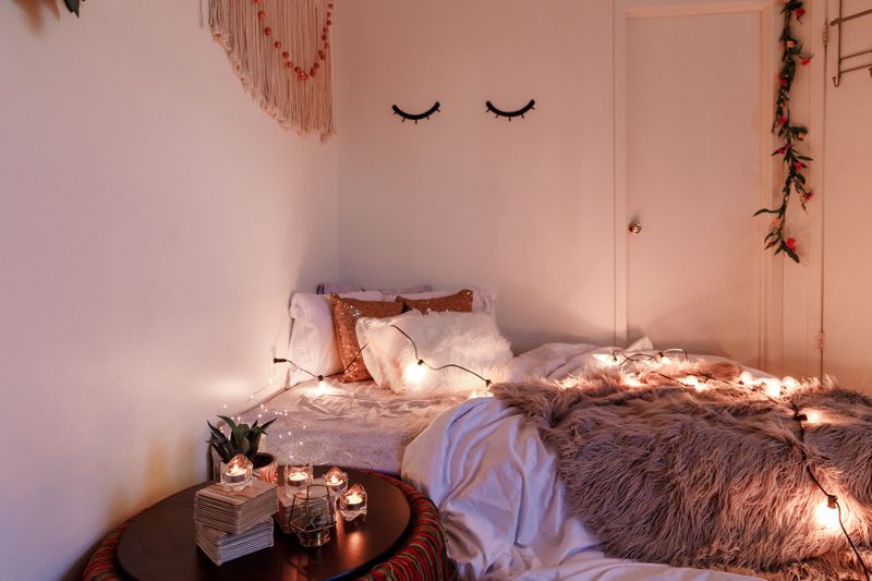 A small bed with fluffy pillows, string lights, and earthy wall decorations