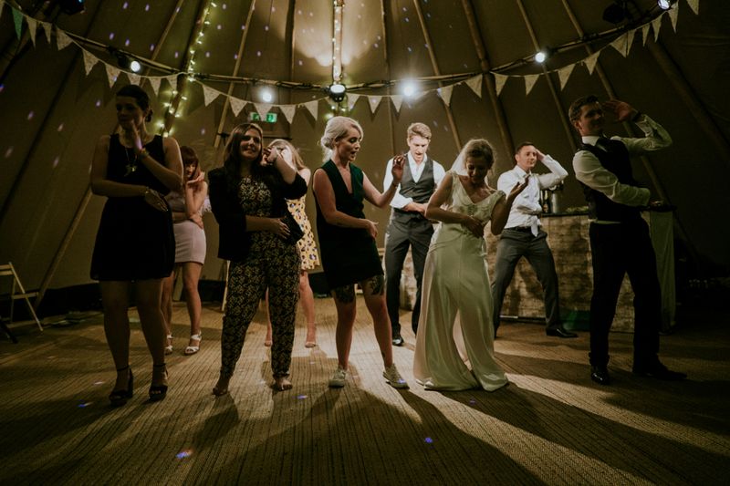 A small wedding party of people dancing in a tent.