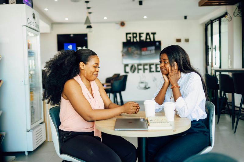 Two women in a cafe. Their devices are closed and on the table, and they make eye contact as they speak.