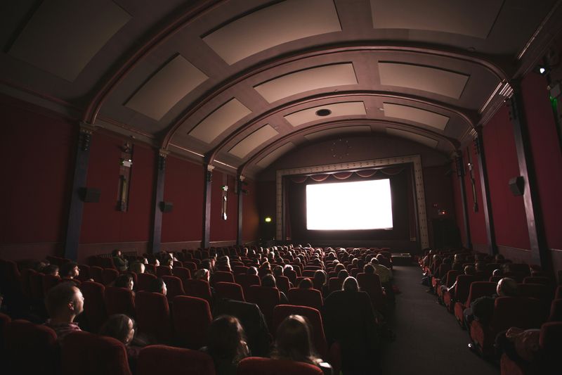 Movie theatre with a bright white screen and people sitting in seats. 