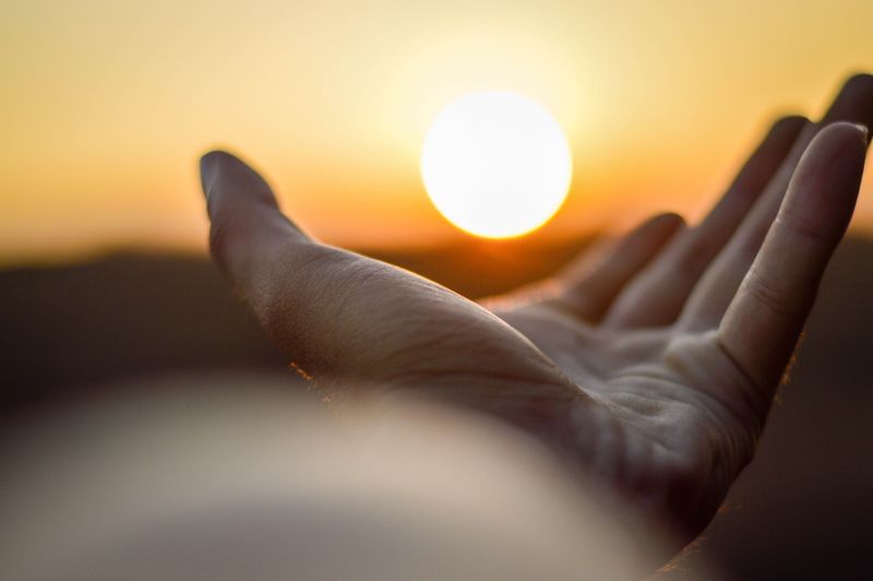 A hand reaching for the sun, giving the illusion that the sun is about to be grasped by the hand.