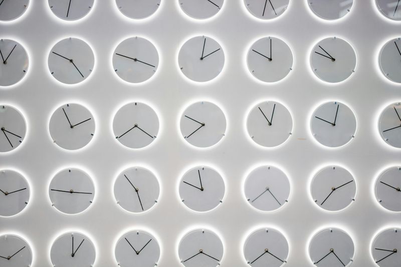 Numerous clocks on a wall with different times displayed.