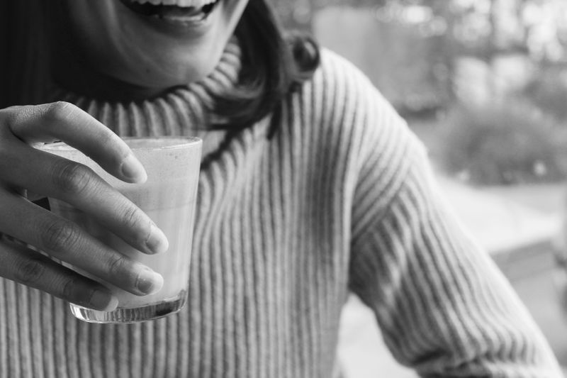 A woman wearing a sweater in a cafe, smiling while having a drink.