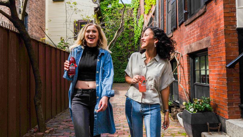 Two happy women walking down a path with drink bottles in their hands.