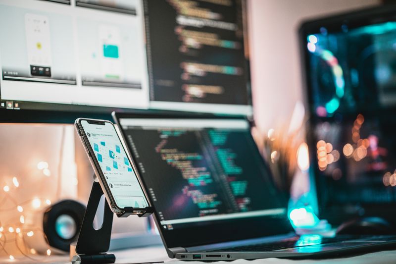 A blurred out computer screens on a desk beside a mobile phone in a stand.