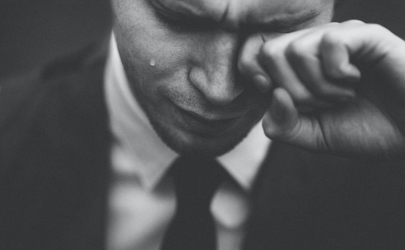 Male crying, holding his hand to on eye to wipe a tear