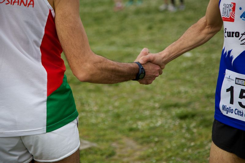 Two runners shaking hands in a field.