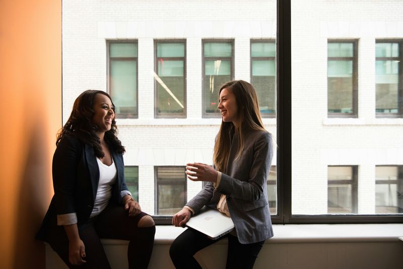 Two women having a conversation by a window.