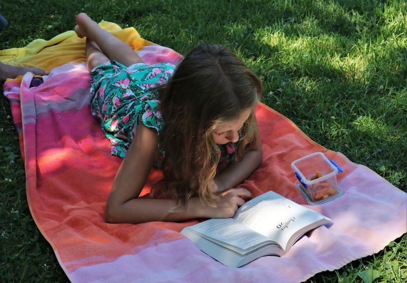 Older child laying outdoors on grass reading a book