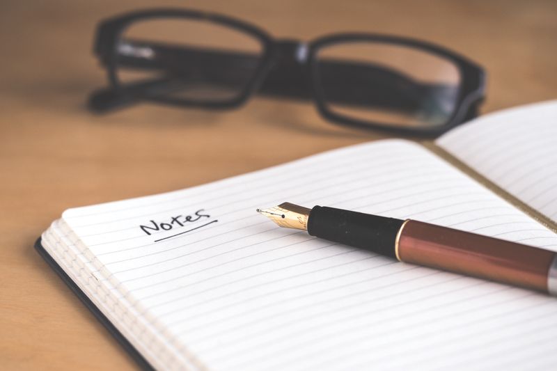 Image of a notepad and fountain pen. 'Notes' is written at the top of the page and a pair of glasses are on the table.