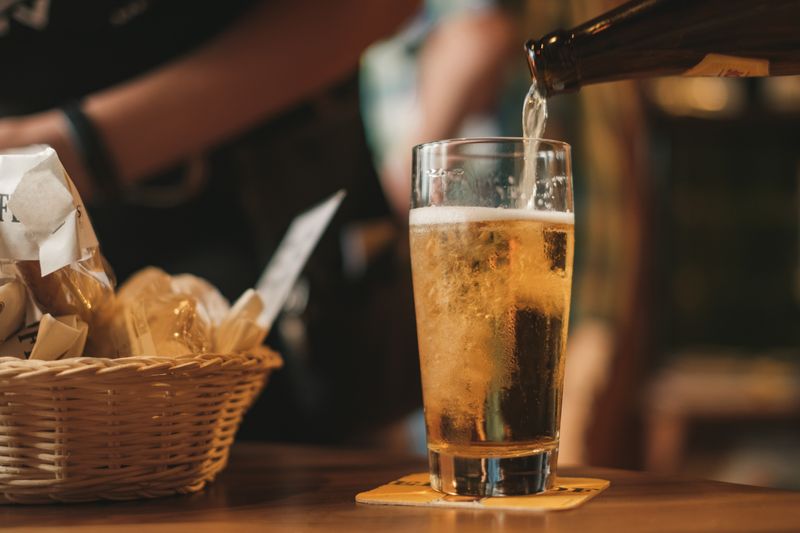 A beer is poured into a glass next to a basket of bread at a restaurant.