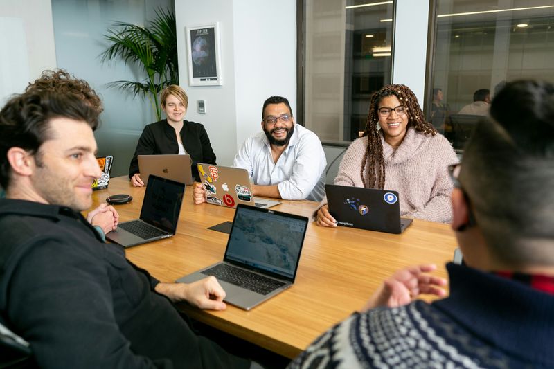 A group of people sitting around a large table, holding a meeting. 