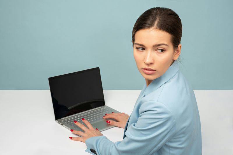 A woman on her laptop looking behind her with a fearful expression.