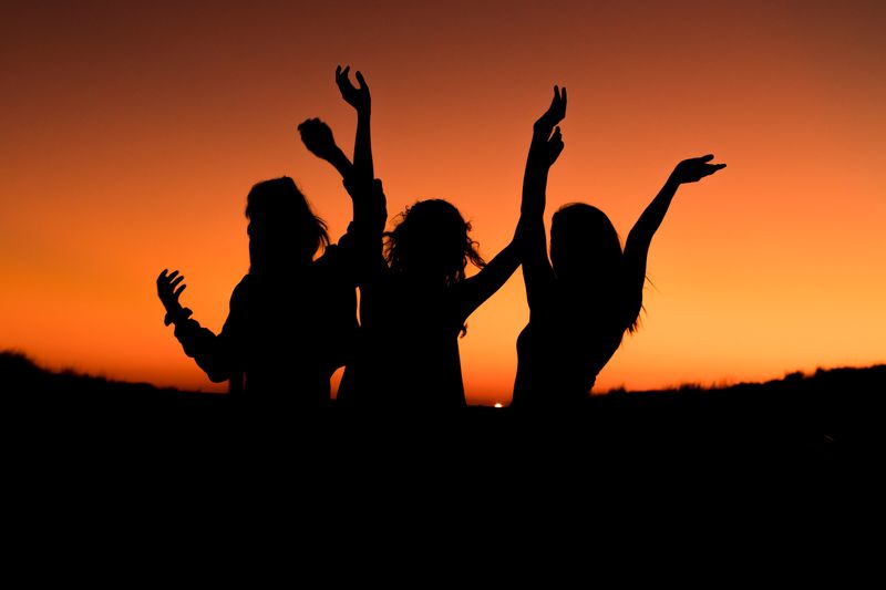 Silhouettes of three people dancing in a field at twilight.